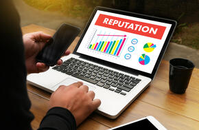 Over shoulder view of laptop with red 'Reputation' banner on screen.