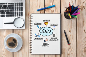 Desktop with computer, pens, coffee and pad with SEO cloud diagram.